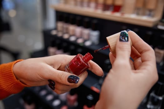 Woman hands holding bright red nail polish in cosmetics store. Lady choosing decorative cosmetics in shop