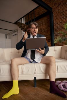 Portrait of funny businessman wearing formal suit and cute socks with different color working online on laptop. Concentrated salesman sitting on sofa using computer for internet job