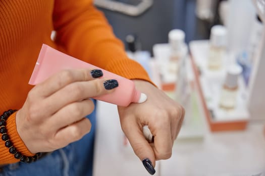 Lady testing hand cream on her skin. White consistence in pink tube