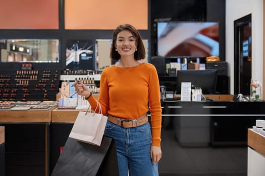 Beautiful woman customer holding shopping bags in cosmetics shop. Satisfying lady with new purchases