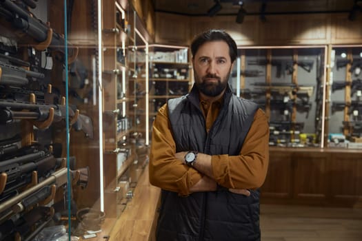 Pensive man choosing rifle gun looking at showcase in store. Armament shopping for hunting