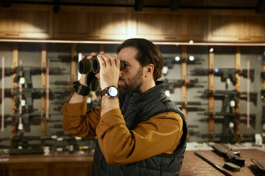 Male client choosing new binocular for hunting while doing purchase in modern weapon shop. Armament retail concept