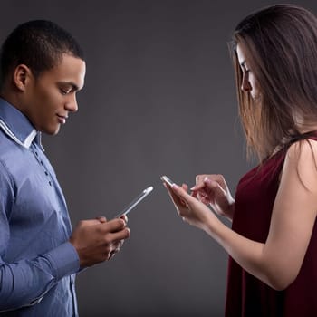 Young couple standing together, absorbed in smartphones, showing the challenge of tech addiction in relationships. Grey background symbolizes disconnect caused by excessive phone use