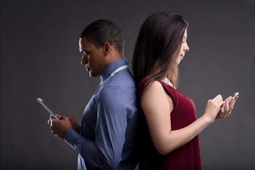 Young couple stands back to back, absorbed in phones, showing challenges of digital communication