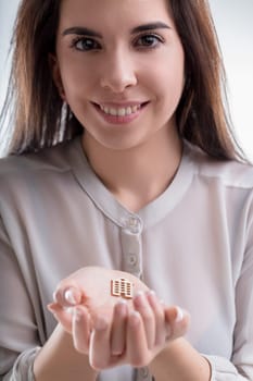 Smiling woman holds a miniature house model in her hands. The scene connects to real estate, home buying, love for ones home, insurance, and financial topics, emphasizing care and security in homeo