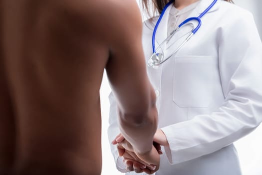 Doctor wearing a white coat and stethoscope is holding the hands of her patient, offering comfort and reassurance during a difficult time