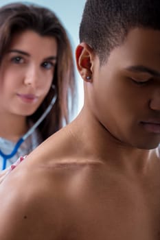 Female doctor is holding a stethoscope to a male patient's chest, listening to his heart and lungs during a medical checkup