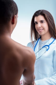 Smiling female doctor examines a male patient's back with a stethoscope in a hospital setting. Exuding care and expertise. The patient. An adult man of african descent. Trusts the doctor's diagnosis