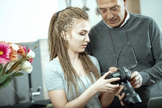 Senior photographer teaches a young woman how to use a professional camera, sharing knowledge and skills in a photography studio