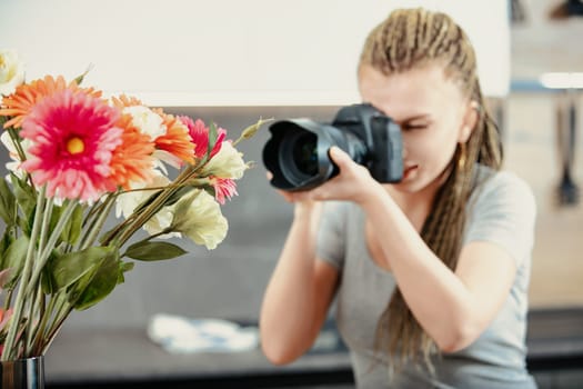 Young female photographer with braided hair focuses her camera on a vibrant bouquet of flowers. The flowers are sharply in focus, highlighting their colors and details, while she works intently in the