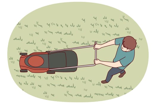 Man uses lawn mower to cut grass and wild weeds on golf course in park or in own backyard. Top view of young guy dressed in casual clothes with lawn mower working as gardener or janitor.