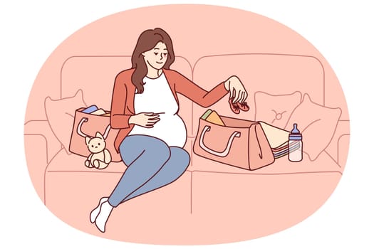 Pregnant woman is packing things for unborn child in bag going to maternity hospital before giving birth. Pregnant girl is sitting on couch getting ready for motherhood and raising baby
