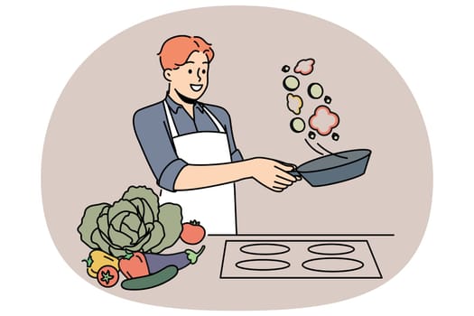 Man cook stands at stove and prepares romantic dinner of fried vegetables for beloved woman. Chef cook guy throws food on pan demonstrating skills of professional culinary specialist