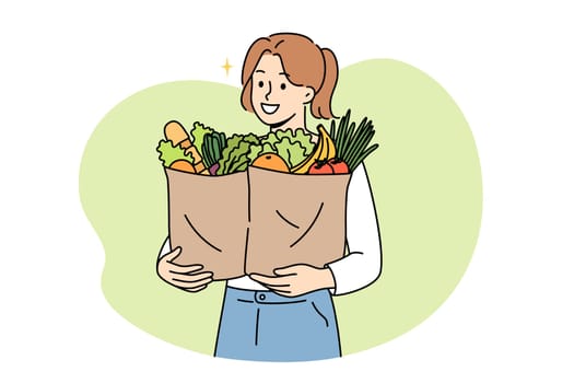 Vegan woman proudly carries paper bags with natural vegetables and fruits bought at farmers fair. Vegan girl buys only organic plant products grown without use of pesticides and nitrates