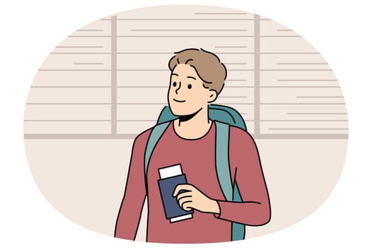 Man tourist stands at airport near board of upcoming flights and holds passport and plane ticket. Guy passenger of airport with backpack behind back is going on trip and waiting for flight