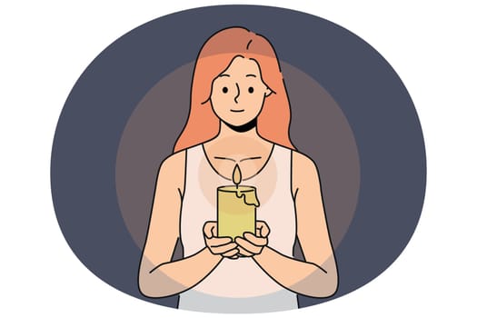 Woman with candle in hands looks at fire, performing religious ritual or seance. Positive girl holding candle to light way in dark due to power outage in house or broken lighting fixtures