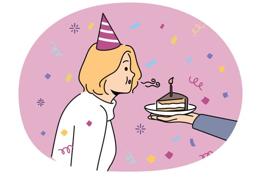 Birthday woman blows out candle on piece of cake celebrating anniversary and making cherished wish. Girl in birthday hat stands among confetti celebrating day of angel and dreaming about future