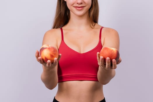 Happy cheerful a young blond woman holding nectarines in hands over chest