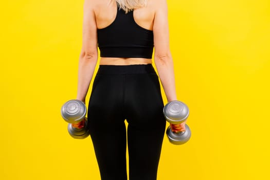 Sporty woman does exercises with dumbbells on dark, yellow, red background.