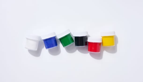 Plastic jars with multi-colored gouache on a white background, top view