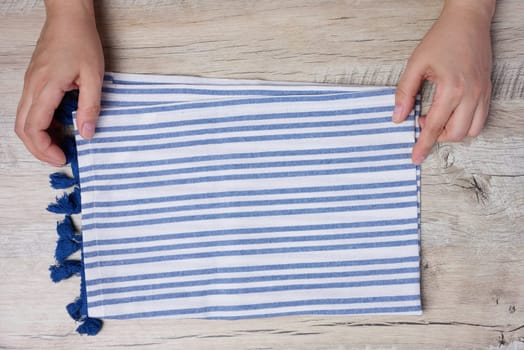Two female hands hold a white and blue striped kitchen towel on the table, top view