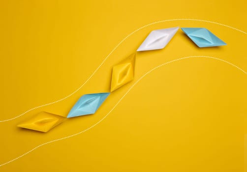 Paper boats on a yellow background, top view, representing the concept of unity and achieving common goals. Top view