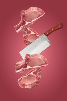 Raw pieces of pork on the bone and a cutting knife levitate on a red background