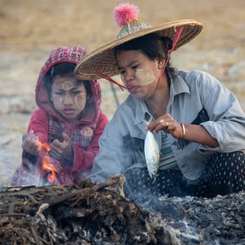 A Burmese mother and daughter cooking a fish on Nagapali Beach in Rakhine State in Myanmar (Burma).