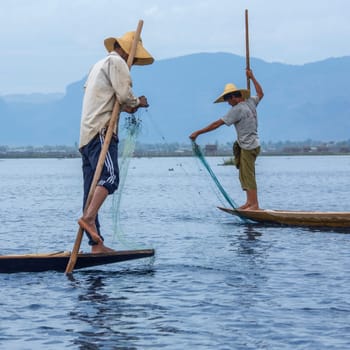 Leg rowing fisherman in the dawn light on Inle Lake in Shan State, Myanmar (Burma). This unique style of rowing evolved because the shallow lake bottom is covered by reeds and plants making it difficult to see the fish while sitting. Standing gives a better view.