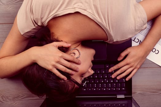 Overwhelmed by exhaustion, a woman rests her head on her laptop after working on a contract. Her posture highlights the physical toll of extensive work and the struggle to keep going