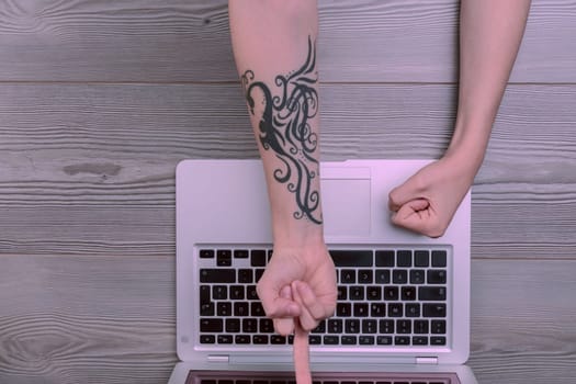 Two hands, one tattooed, are poised in frustration or triumphant revenge over a laptop, symbolizing the struggle and conflict with technology that often complicates rather than simplifies life