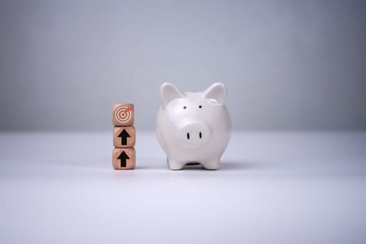 Piggy bank and wooden blocks with dart board and arrow icons on them and white background, Saving money and financial plan for investment concept, Business and financial goals.