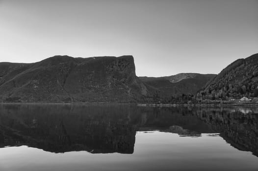 Norwegian fjord landscape. Mountains with rugged vegetation in black and white. Crystal clear water