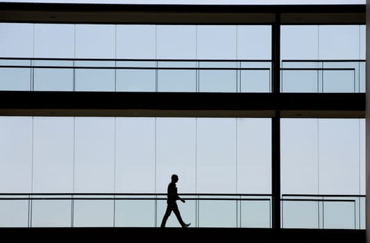 Silhouette view of young businessman walking in modern office building interior with panoramic windows.
