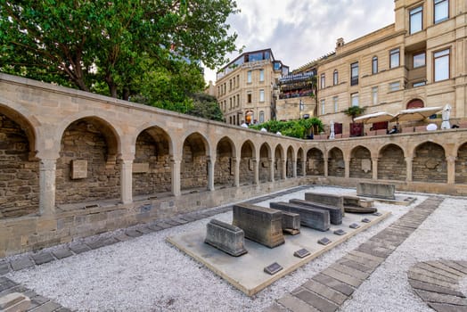 The Khanqah complex courtyard in Baku's Old Town, aka Icherisheher, Azerbaijan, features stone arches and ancient artifacts displayed on a platform