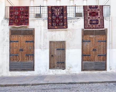 Three colorful carpets hang above vintage wooden doors outside a building in Old Town, Baku, Azerbaijan during the inaugural National Carpet Festival