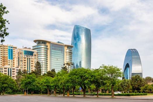 Modern skyscrapers and lush greenery frame a bustling street in Baku, Azerbaijan. The Crescent Development Project's iconic towers stand tall against a clear blue sky