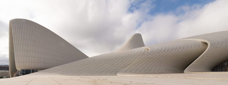 The iconic Heydar Aliyev Centre in Baku, Azerbaijan, showcases modern architecture with its fluid, wave-like design against a cloudy sky. Building designed by architect Zaha Hadid