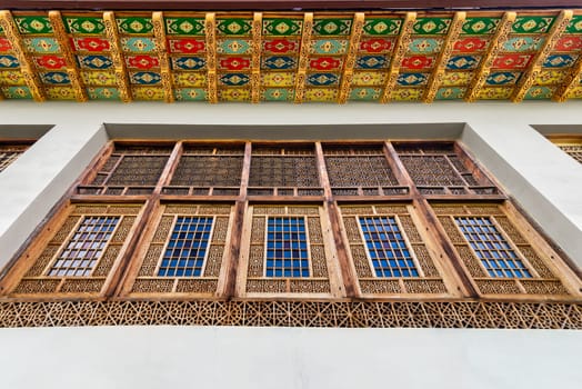 Intricate wooden window at the Shakikhanovs Palace in Shaki, Azerbaijan, are framed by a colorful patterned ceiling