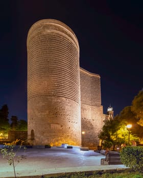 The iconic Maiden Tower stands illuminated against a night sky in Baku, Azerbaijan, with lush greenery in the foreground