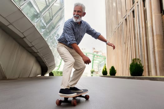 Active energetic happy cool gray haired old adult man skateboarding on city street, smiling sporty fit middle aged mature older male professional skater having fun enjoying riding skateboard outdoor.