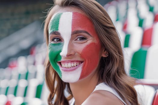 Smiling happy woman, fan of the Italian team in the stands of the stadium with the painted Italian flag on her face.