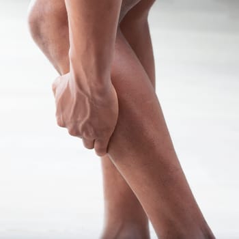 Close-up of a man grasping his lower leg, suggesting pain or muscle cramp. The image captures the tension in his calf muscles and his feet, which are positioned to relieve strain