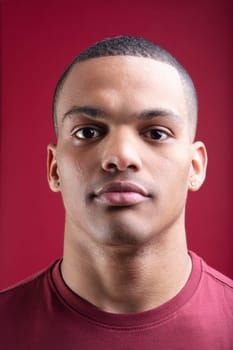 Serious young man with short hair and a red t shirt stands against a vibrant red background, exuding confidence and masculinity