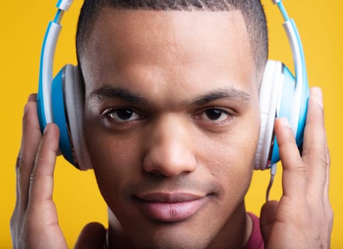 Young man happily listening to music with headphones in a colorful studio shot. The yellow background adds a modern touch to his serene expression