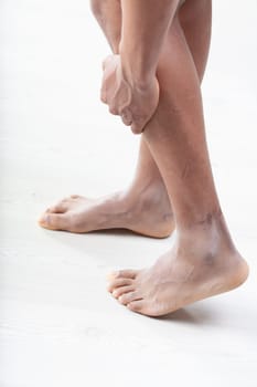 man clutches his lower leg with one hand, indicating possible calf pain or muscle cramp. His feet are positioned to suggest discomfort, and the background is softly blurred to emphasize the area of pa