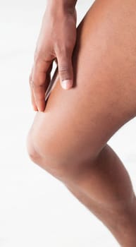 mans hand is firmly pressing his thigh, suggesting pain or muscle strain. His feet are positioned to show discomfort, with one foot slightly raised, and the background is softly blurred