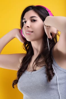 Beautiful young woman with brunette hair dances happily while listening to music on headphones against a vibrant yellow background