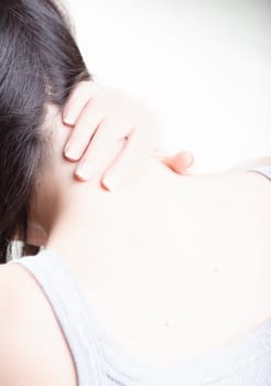 woman holds her neck with one hand, indicating possible neck pain or discomfort. The close-up emphasizes the tension in her hand and neck, with a blurred background for focus
