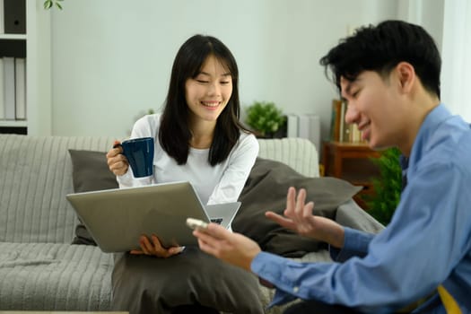 Happy young couple relaxing on a couch using laptop and smartphone.